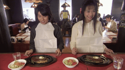 A Man And A Woman Sit At A Table With Plates Of Food And A Sign That Says 30 GIF