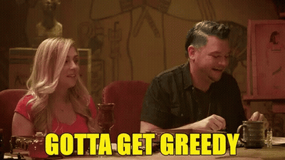 A Man And A Woman Sit At A Table With The Words Gotta Get Greedy GIF