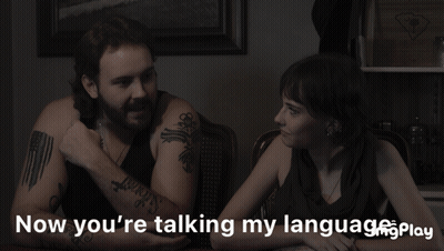 A Man And A Woman Sit At A Table With The Words Now You 'Re Talking My Language Play GIF