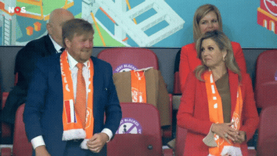 A Man And A Woman Sit In A Stadium With Seat Blocks Written On The Backs Of Their Seats GIF