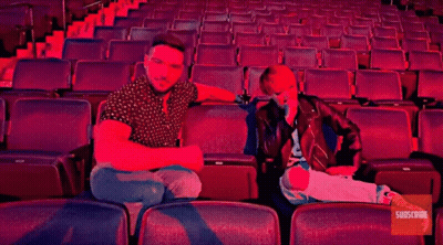 A Man And A Woman Sit In An Empty Auditorium With The Words Buc-Ee 'S GIF