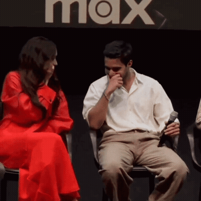 A Man And A Woman Sit In Front Of A Max Sign GIF