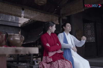 A Man And A Woman Sit Next To Each Other In Front Of A Youku Logo GIF
