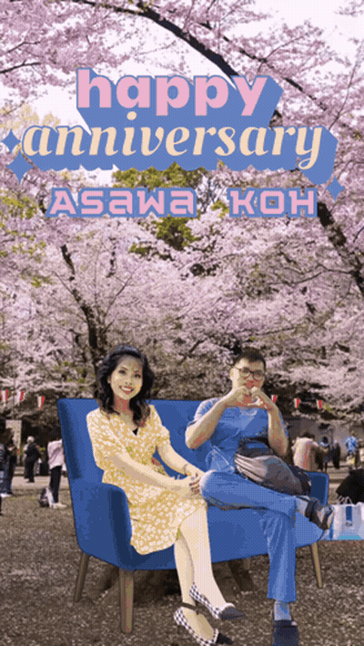 A Man And A Woman Sit On A Blue Couch In Front Of Cherry Blossom Trees And The Words Happy Anniversary GIF