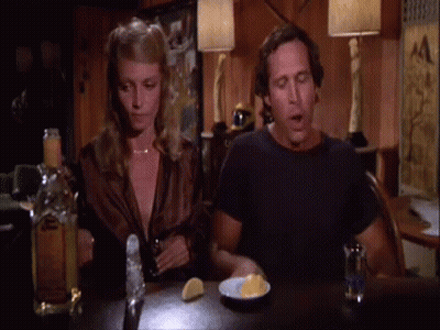 A Man And A Woman Sitting At A Table With A Bottle Of Tequila GIF