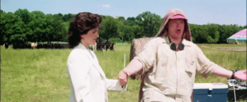 A Man And A Woman Standing In A Field With A Blue Cooler In The Foreground GIF