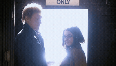 A Man And A Woman Standing In Front Of A Sign That Says Only GIF