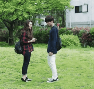A Man And A Woman Standing Next To Each Other In A Park . GIF
