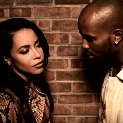 A Man And A Woman Standing Next To Each Other In Front Of A Brick Wall GIF
