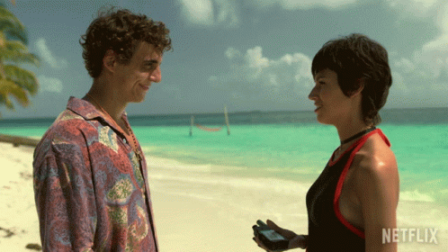 A Man And A Woman Standing On A Beach With Netflix Written On The Bottom GIF