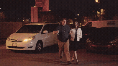 A Man And A Woman Walking In Front Of A Burning Van GIF