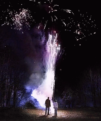 A Man And A Woman Watch Fireworks In The Night Sky GIF