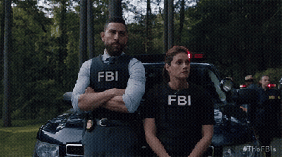 A Man And A Woman Wearing Fbi Vests Standing In Front Of A Car GIF