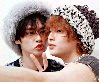 A Man And A Woman Wearing Fur Hats Are Making A Peace Sign GIF