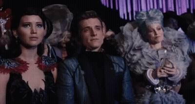 A Man And Two Women Are Sitting In A Crowd Looking At Something GIF