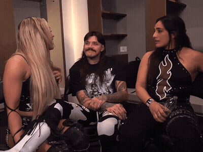 A Man And Two Women Are Sitting In A Room And The Man Has A Tattoo On His Arm That Says ' X ' On It GIF