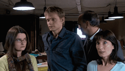 A Man And Two Women Are Standing In A Dark Room With Lamps Hanging From The Ceiling GIF