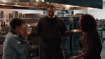 A Man And Two Women Are Standing In A Kitchen And The Man Is Smiling GIF