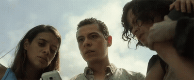 A Man And Two Women Look At A Cell Phone Together GIF