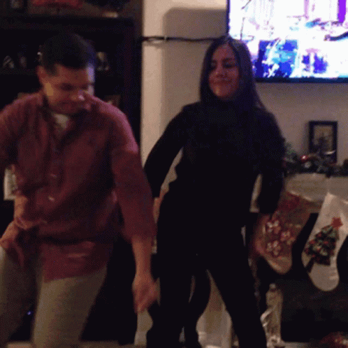 A Man And Woman Are Dancing In Front Of A Tv GIF