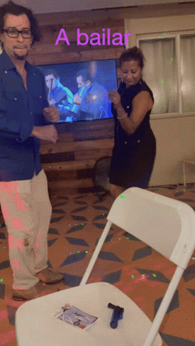 A Man And Woman Are Dancing In Front Of A Tv That Says A Bailar On It GIF