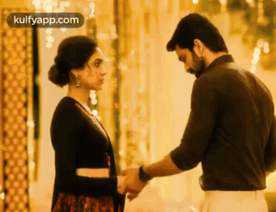A Man And Woman Are Holding Hands And Looking At Each Other . GIF