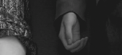 A Man And Woman Are Holding Hands In A Black And White Photo . GIF