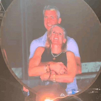 A Man And Woman Are Hugging Each Other In Front Of A Sign That Says M GIF