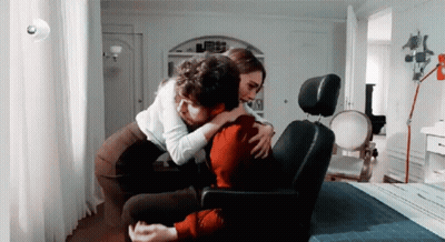 A Man And Woman Are Hugging Each Other While Sitting In A Chair . GIF