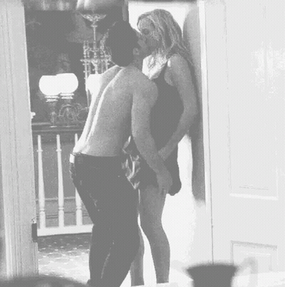 A Man And Woman Are Kissing In A Doorway . GIF