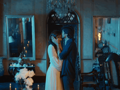 A Man And Woman Are Kissing In A Room With Candles GIF