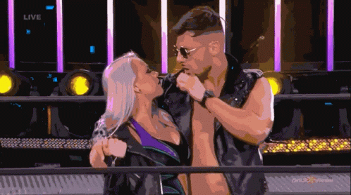 A Man And Woman Are Kissing In Front Of A Sign That Says Live On It GIF