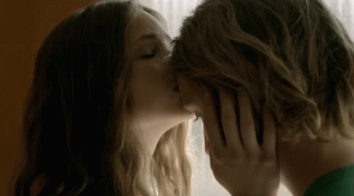 A Man And Woman Are Kissing In Front Of A Window . GIF