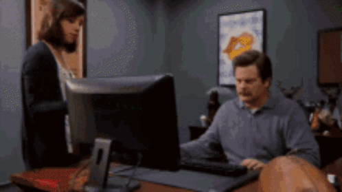 A Man And Woman Are Looking At A Computer Screen GIF