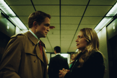 A Man And Woman Are Looking At Each Other In A Hallway GIF