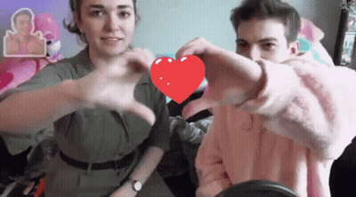 A Man And Woman Are Making A Heart Shape With Their Hands GIF