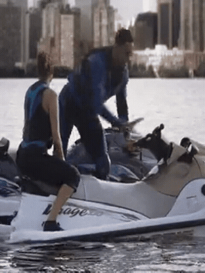 A Man And Woman Are Riding A Jet Ski That Says Voyage GIF