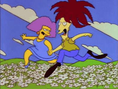 A Man And Woman Are Running Through A Field Of Flowers GIF