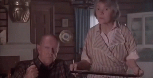 A Man And Woman Are Sitting At A Table In A Living Room . GIF