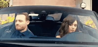 A Man And Woman Are Sitting In A Car . GIF