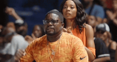 A Man And Woman Are Sitting In The Stands At A Basketball Game . The Man Is Wearing Glasses And A Nike Shirt . GIF