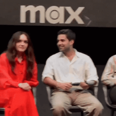 A Man And Woman Are Sitting Next To Each Other In Front Of A Max Sign . GIF