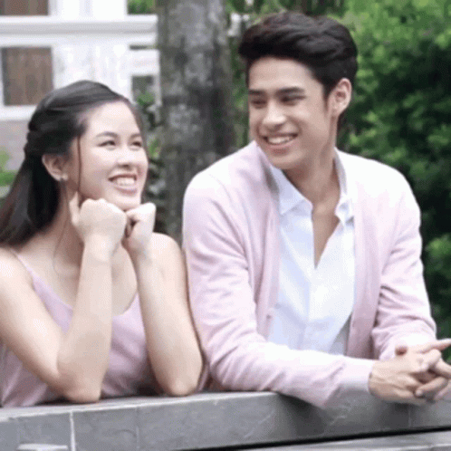 A Man And Woman Are Sitting Next To Each Other On A Bench And Smiling . GIF
