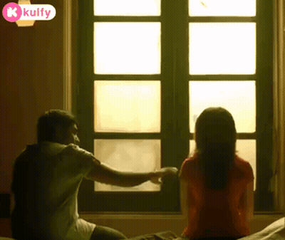 A Man And Woman Are Sitting On A Bed Looking Out A Window . GIF