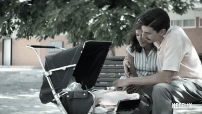 A Man And Woman Are Sitting On A Bench With A Baby In A Stroller And A Netflix Logo In The Corner GIF