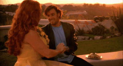A Man And Woman Are Sitting On A Bench With A Plate Of Food In Front Of Them GIF