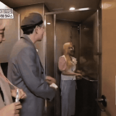 A Man And Woman Are Standing In An Elevator With A Sign That Says ' Elevator ' On It . GIF