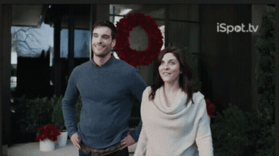 A Man And Woman Are Standing In Front Of A Building With A Wreath In The Background And Ispot.tv On The Bottom Right GIF