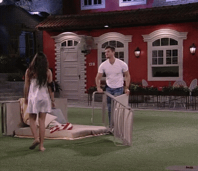 A Man And Woman Are Standing In Front Of A Red House With The Number 178 On The Front GIF