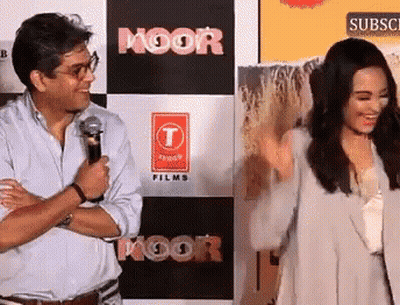 A Man And Woman Are Standing In Front Of A Sign That Says Moor Films GIF
